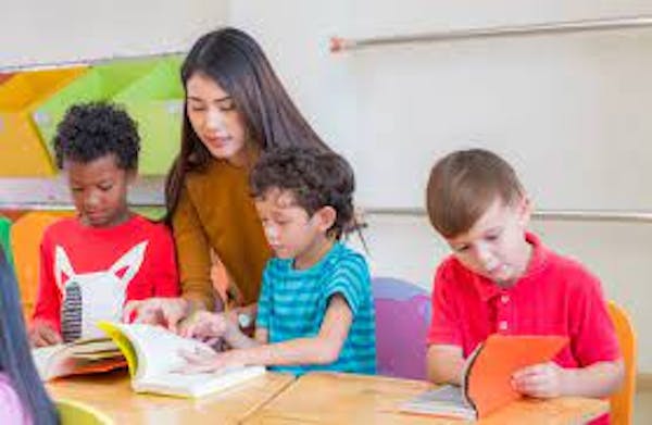 One teacher with three students at a table reading books