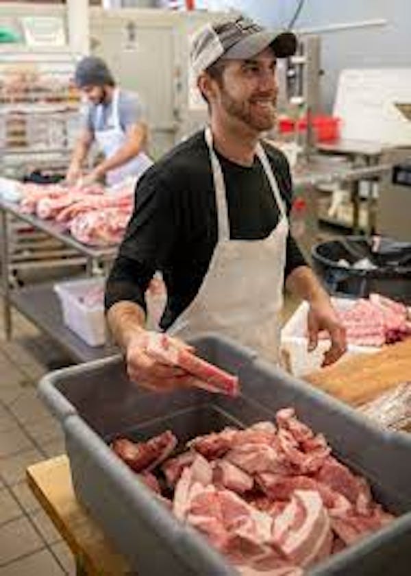 Person wearing apron sorting cuts of meat in grocery setting