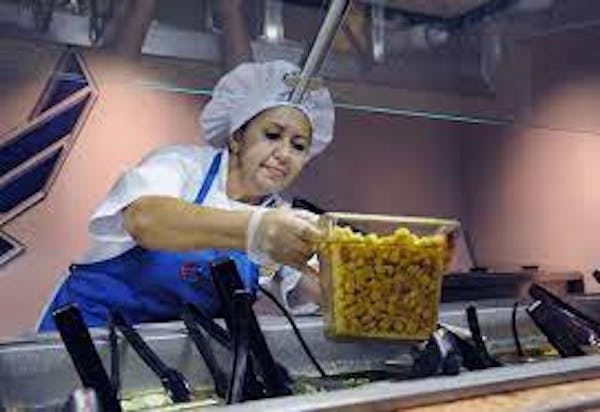 Person with apron and hairnet placing cold food item on salad bar