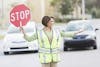 Person wearing yellow vest and holding stop sign directing at a cross walk