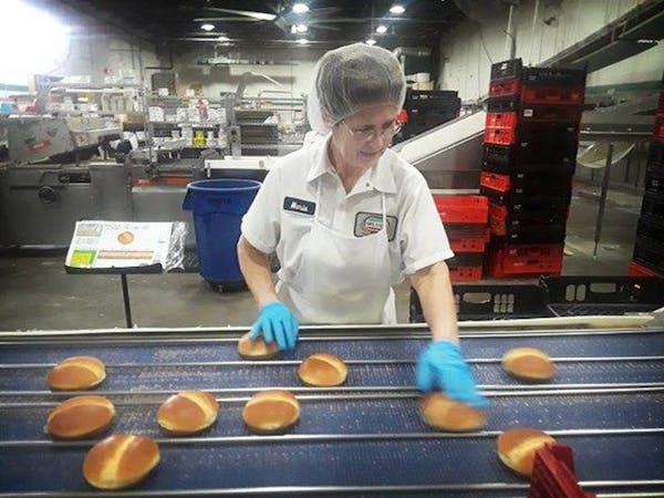 Person wearing uniform, hairnet and gloves separating bread products on assembly line