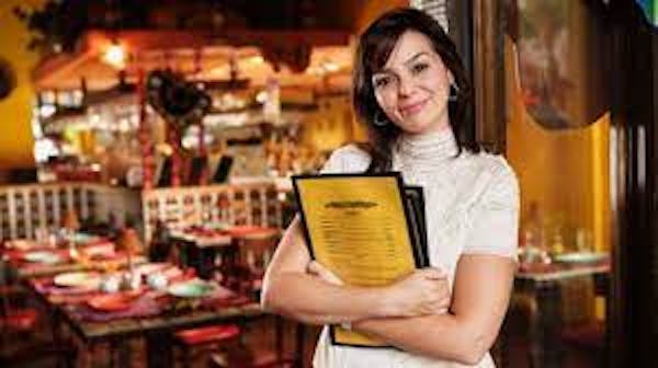 person holding orange/yellow menus wearing a white short-sleeved turtleneck in a restaurant