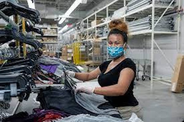 Person wearing a mask holding clothes for merchandising in a warehouse environment.