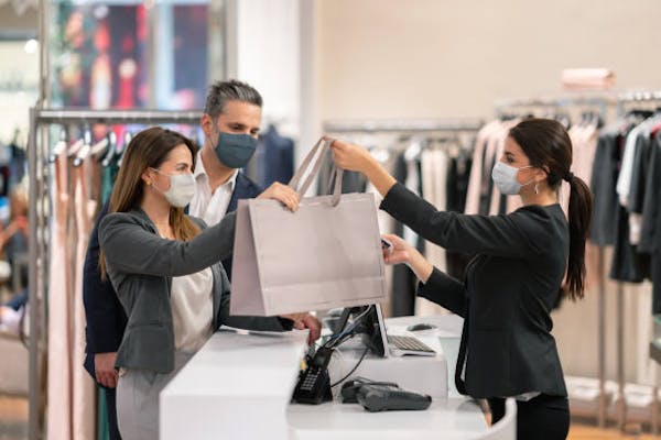 Woman handing a large retail bag to a female and male customer in a clothing store,