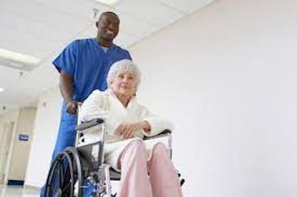 Individual in blue scrubs pushing individual in wheelchair