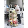 Image of a man wearing a white chef's coat, while stacking  produce onto a dolly that already has bagged onions, and boxes of corn and other produce.