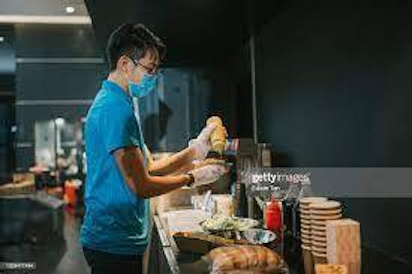 Person preparing a hot dog in a concession stand for customer,