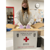 Person wearing white uniform and gloves packing a box with red cross on front