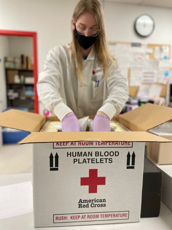 Person wearing white uniform and gloves packing a box with red cross on front