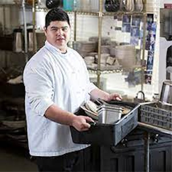Man in chefs coat holding bus tub with dishes
