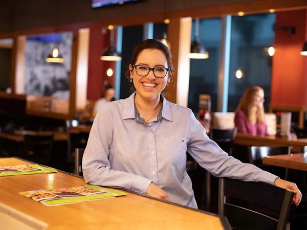 Person greeting cutomers with a smile. leaning on a wood bar, in a restaraunt