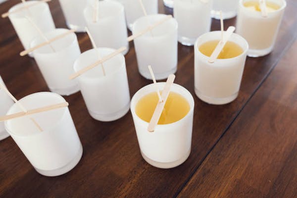 A table with a bunch of empty white candle votive containers & a few in the front that have been filled with wax & a wick that is being supported by a stick (to hold it in place).