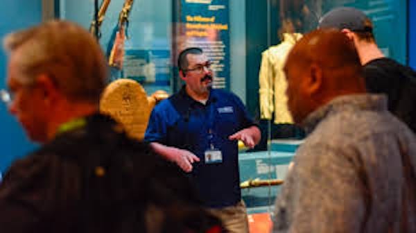 Person with a polo shirt and employee lanyard talking to group at museum
