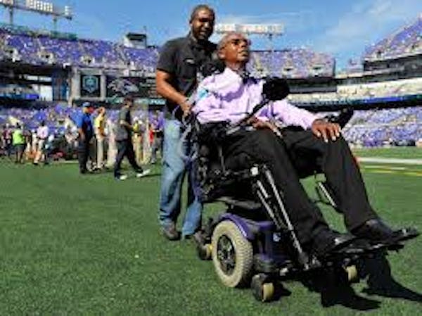 Person pushing another person in a wheelchair in a stadium setting