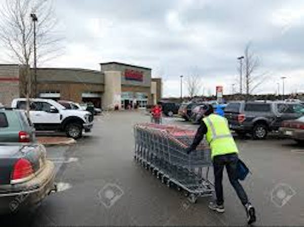 Person pushing carts in a parking lot wearing a yellow safety vest