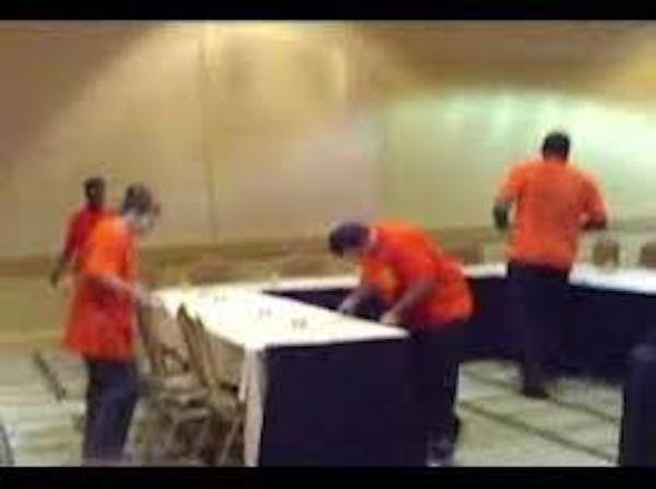People setting up banquet room with tables and placing linens on table tops