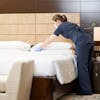 Person in scrubs making bed in hotel room