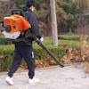 Person utilizing a backpack power blower to clear leaves on surface