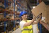 Person in a warehouse wearing a hardhat, stocking items into a cardboard box