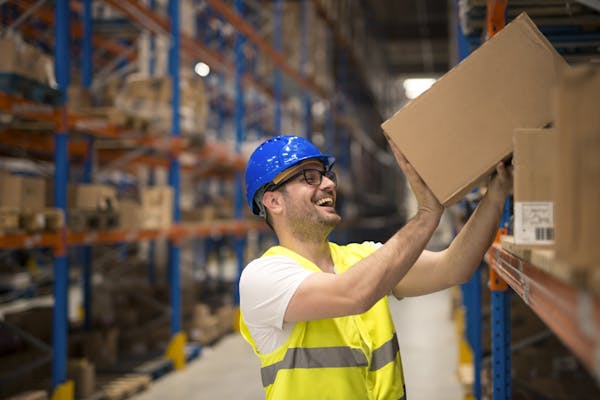 Person in a warehouse wearing a hardhat, stocking items into a cardboard box