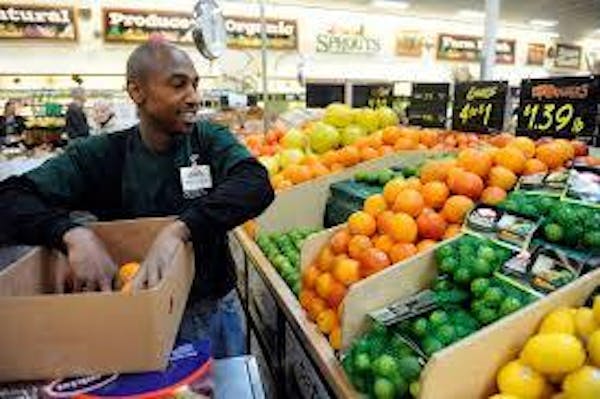 Person holding a box of fruit in front of a produce display staging stocking product