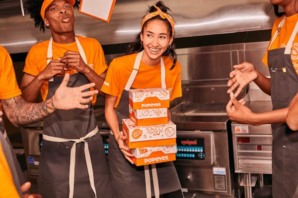 4 Popeyes team members in kitchen - one holding 4 boxes of popeyes branded chicken