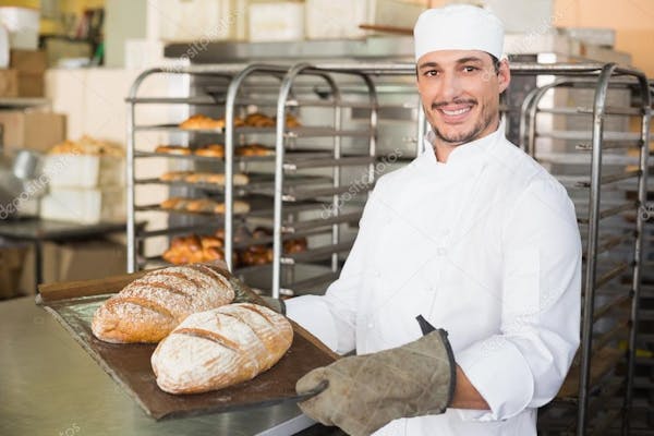 Person smiling in white baking jacket & hat showing baked goods.