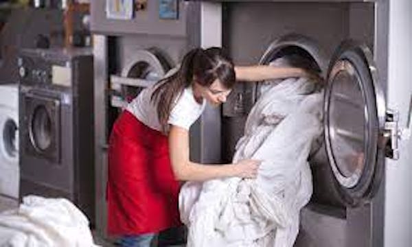 Person unloading white linens from industrial-sized clothes dryer