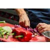 Person using a knife to cut a purple onion on a red cutting board with red bell peppers nearby