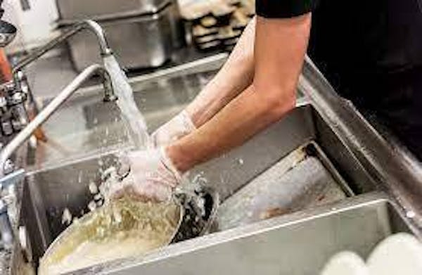 Hands wearing gloves and washing pots under running water in a 3-compartment sink