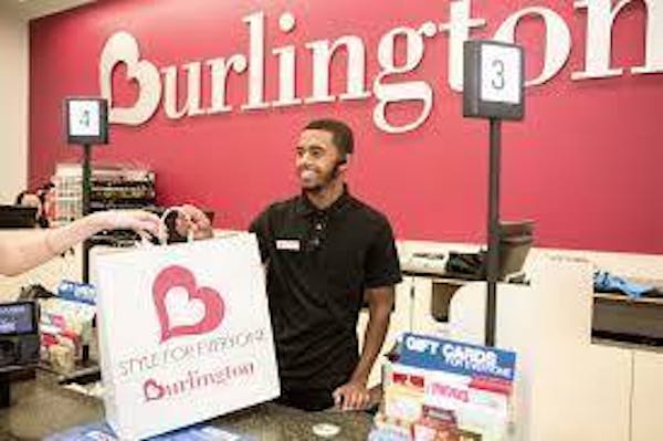 Person smiling handing a white bag with red letters spelling "Burlington" behind a POS register system.
