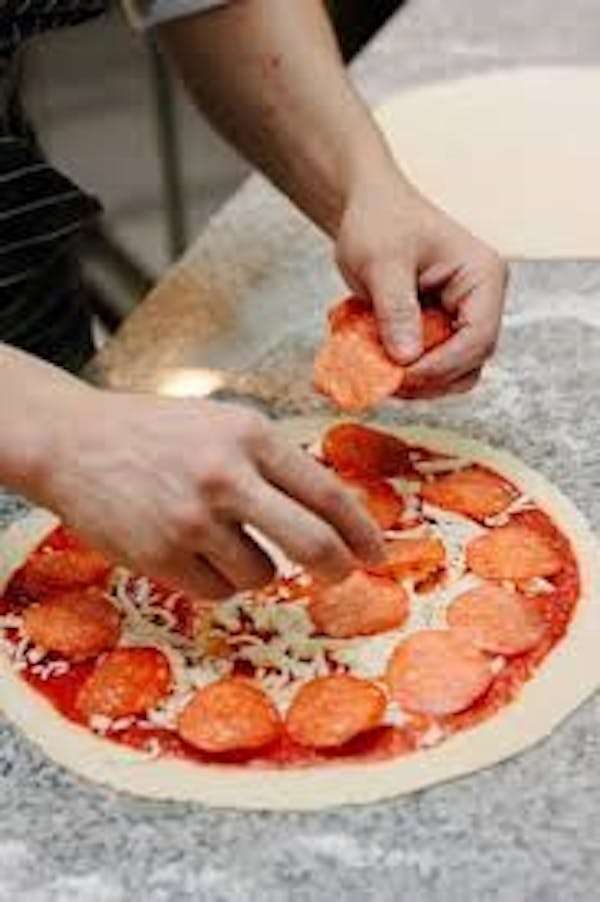 Person placing pepperoni on pizza dough