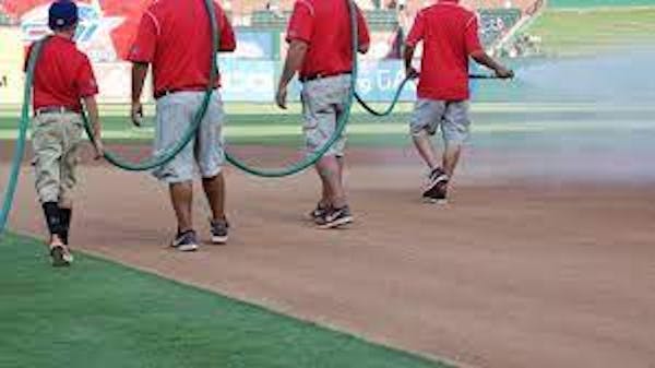 Crew holding a hose spraying field at professional baseball ballpark