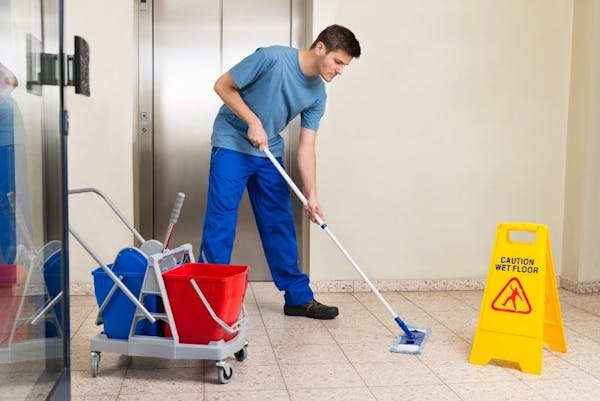 Person in scrubs mopping floor with caution sign and bucket on ground