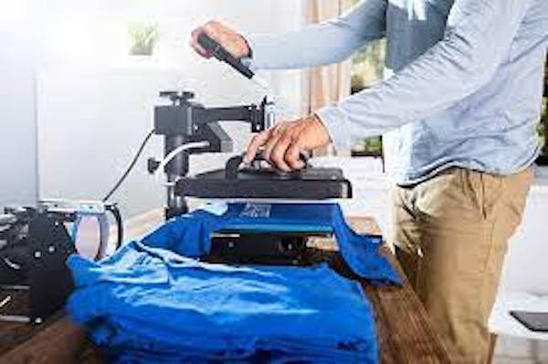 Person using a heat-press machine to print logos on blue t-shirts