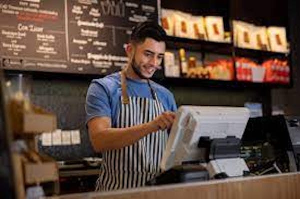 Person with apron on checking out guest at cash register