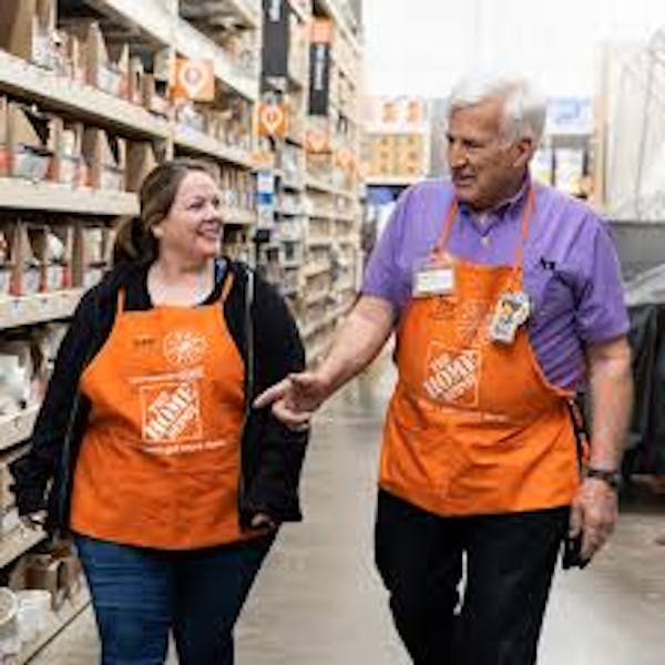 Two people in Home Depot aprons talking in aisles of store