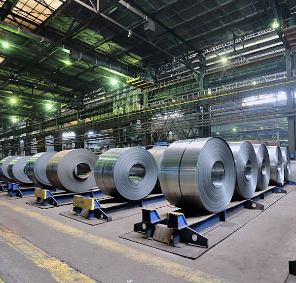 A large warehouse with enormous rolls of sheet metal lined up in rows.