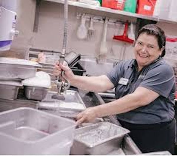 Person smiling while spraying pans in a dishwashing area