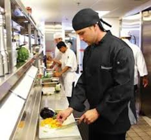 Person wearing a black chef coat and hat chopping food on a cutting board