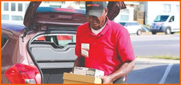 Person in red shirt with boxes walking away from car