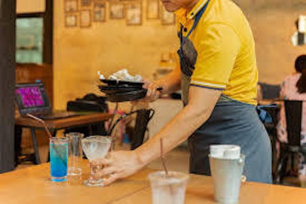 Person clearing a table of glasses and dishes 