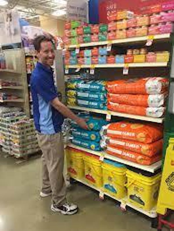 Person wearing a blue shirt smiling and putting dog food on a shelf.