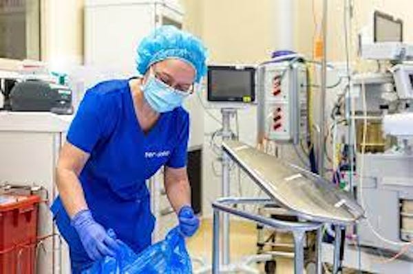 Person wearing scrubs, mask, gloves and hair net cleaning in a medical setting.