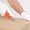 Person with white gloves using a box cutter, cutting open a box
