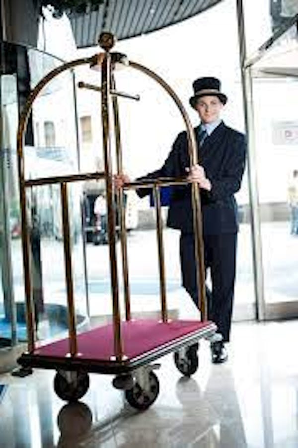 Person wearing bellman uniform pushing luggage cart in hotel environment
